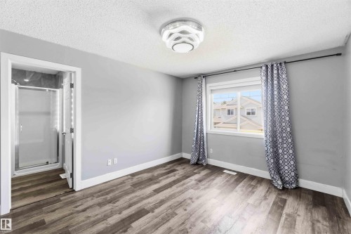 Light-filled room featuring wood-finish flooring, a contemporary ceiling light fixture, and a built-in shower enclosure with a glass door - #64 120 Magrath Rd Nw, Edmonton, AB - Indoor Photo Showing Other Room