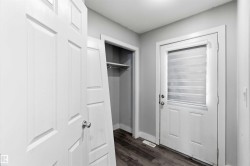 Entryway featuring a white paneled door with round silver hardware, a closet with shelving and a hanging rod, a white exterior door with an inset privacy blind, and wood-finish flooring - 