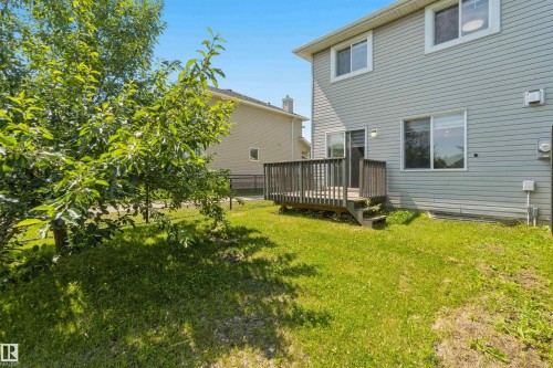 Expansive backyard featuring a wood deck with steps, a sliding glass door for outdoor access, and mature trees - #64 120 Magrath Rd Nw, Edmonton, AB - Outdoor