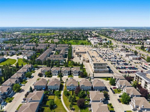 Expansive aerial view showcasing residential properties, a commercial complex with extensive parking, and a multi-lane roadway - #64 120 Magrath Rd Nw, Edmonton, AB - Outdoor With View
