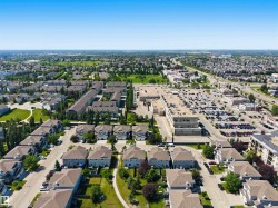 Expansive aerial view showcasing residential properties, a commercial complex with extensive parking, and a multi-lane roadway - 