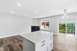 Kitchen island with white cabinetry and a light-toned countertop, wood-finish flooring, recessed lighting, and a fireplace with a dark stone surround and white mantle - 