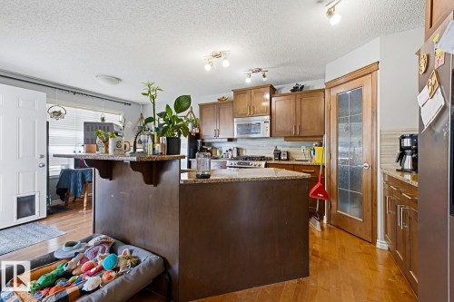 Kitchen featuring wood-finish flooring, wood cabinetry, stone countertops, and stainless steel appliances - 3724 163 Avenue Nw, Edmonton, AB - Indoor Photo Showing Kitchen