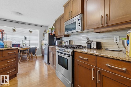 Kitchen featuring wood-finish cabinetry with modern hardware, stone-finish countertops, and a tiled backsplash - 3724 163 Avenue Nw, Edmonton, AB - Indoor Photo Showing Kitchen