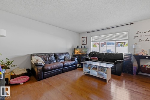 Living area featuring wood-finish flooring, white walls, and a large window with horizontal blinds - 3724 163 Avenue Nw, Edmonton, AB - Indoor Photo Showing Living Room