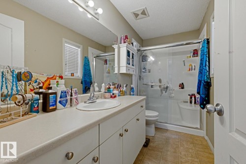 Bathroom featuring a single vanity with an integrated sink, a large mirror, a shower with a sliding glass door, and tiled flooring - 3724 163 Avenue Nw, Edmonton, AB - Indoor Photo Showing Bathroom