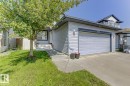 Light-toned siding exterior featuring an integrated garage with panel-style door, a concrete driveway, and a mature front yard tree - 3724 163 Avenue Nw, Edmonton, AB  - Outdoor 
