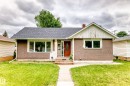 Bungalow-style residence featuring a textured stucco exterior, asphalt shingle roof, and a prominent red entry door with oval glass insert - 12423 75 Street, Edmonton, AB 