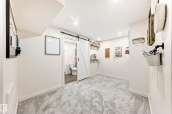 Spacious room featuring light gray carpeting, recessed lighting, white walls, and a white barn door - 
