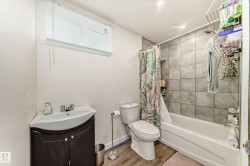 Bathroom featuring a white bathtub, gray tiled shower surround, recessed lighting, and a window with blinds - 