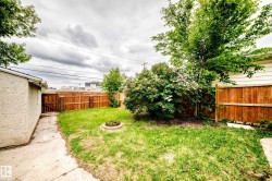 Fenced backyard featuring a concrete pathway, a built-in fire pit, mature trees, and established bushes - 