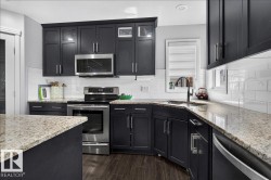 Kitchen featuring dark cabinetry, speckled countertops, stainless steel appliances, white subway tile backsplash, and wood-finish flooring - 