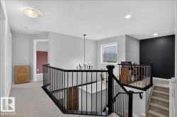 Upper-level hallway featuring light gray wall paint, an open-concept stairwell with black metal railings, a contemporary chandelier, recessed lighting, and a textured accent wall - 