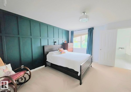 Bedroom featuring a decorative paneled accent wall, a window with blue drapes, and light-colored carpet flooring - 13 Baie Madelene, Beaumont, AB - Indoor Photo Showing Bedroom