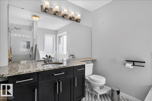 Bathroom featuring a black vanity with a light-toned stone countertop, an undermount sink, and a large wall mirror - 13 Baie Madelene, Beaumont, AB - Indoor Photo Showing Bathroom