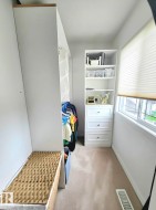 Dedicated closet space featuring white built-in shelving, integrated drawers with decorative pulls, and a window with blinds - 