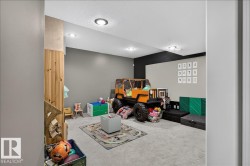 Recessed lighting illuminates a spacious room featuring grey carpeting, two-tone painted walls, and a wood-paneled column - 