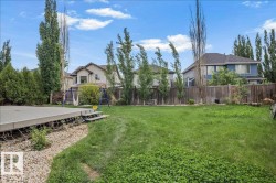 Spacious backyard featuring a composite deck with steps, a gravel border, lush green lawn, and mature perimeter trees - 