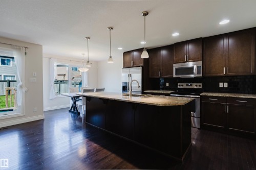 Kitchen featuring a large island with a stone countertop, dark wood-finish cabinetry, stainless steel appliances, and wood-finish flooring - 17348 6 Avenue Nw, Edmonton, AB - Indoor Photo Showing Kitchen With Upgraded Kitchen