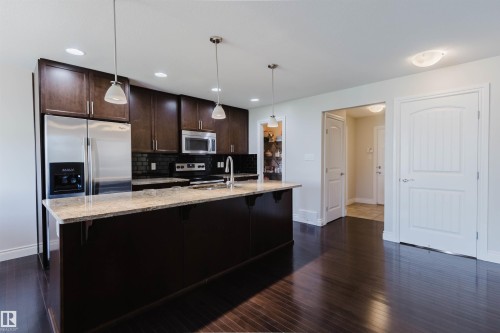 Open-concept kitchen featuring dark wood cabinetry, stainless steel appliances, granite countertops, and a central island with pendant lighting - 17348 6 Avenue Nw, Edmonton, AB - Indoor Photo Showing Kitchen With Upgraded Kitchen