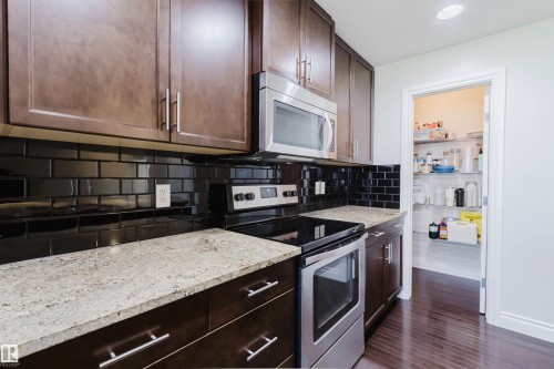 Full kitchen featuring wood-finish cabinetry, light-toned countertops, and a black subway tile backsplash - 17348 6 Avenue Nw, Edmonton, AB - Indoor Photo Showing Kitchen With Stainless Steel Kitchen With Upgraded Kitchen