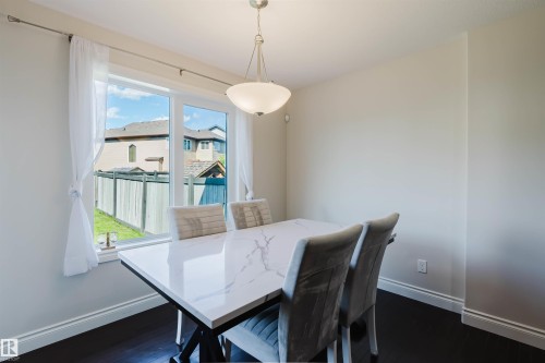 Dining space featuring a large window, dark wood-finish flooring, white baseboards, and a semi-flush mount ceiling light fixture - 17348 6 Avenue Nw, Edmonton, AB - Indoor Photo Showing Dining Room