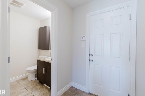 Powder room featuring a dark wood-finish vanity with a white countertop and an integrated sink, a matching wall-mounted cabinet, and large-format tile flooring - 17348 6 Avenue Nw, Edmonton, AB - Indoor Photo Showing Bathroom