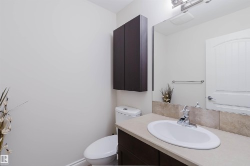 Bathroom featuring a white elongated toilet, dark wood-finish vanity with an oval undermount sink, and light-toned countertop - 17348 6 Avenue Nw, Edmonton, AB - Indoor Photo Showing Bathroom