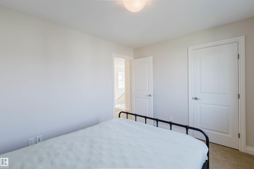 Bedroom featuring light neutral paint, carpet flooring, a flush-mount ceiling light, and white paneled doors with brushed nickel hardware - 17348 6 Avenue Nw, Edmonton, AB - Indoor Photo Showing Bedroom