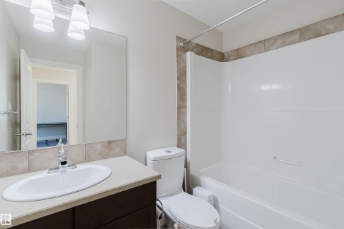 Bathroom with white tub/shower combination, beige tiled surround, and a dark wood-finish vanity with an oval undermount sink - 17348 6 Avenue Nw, Edmonton, AB - Indoor Photo Showing Bathroom