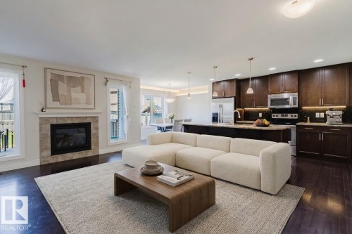 Open-concept living space featuring wood-finish flooring, a tiled fireplace, and multiple windows - 17348 6 Avenue Sw, Edmonton, AB - Indoor Photo Showing Living Room With Fireplace