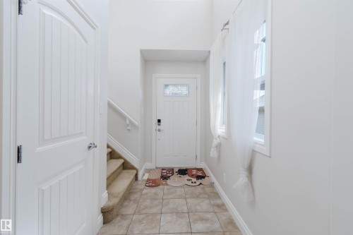 Entryway featuring ceramic tile flooring, a paneled front door with decorative glass insert, and a staircase with carpeted treads and a white handrail - 17348 6 Avenue Nw, Edmonton, AB - Indoor Photo Showing Other Room