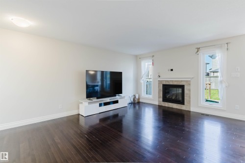 Spacious living area featuring rich wood-finish flooring, a contemporary fireplace with a tiled surround, and crisp white baseboards - 17348 6 Avenue Nw, Edmonton, AB - Indoor Photo Showing Living Room With Fireplace