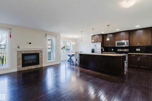 Spacious open-concept interior featuring dark wood-finish flooring, a tile-surround fireplace, and large windows - 17348 6 Avenue Nw, Edmonton, AB - Indoor With Fireplace
