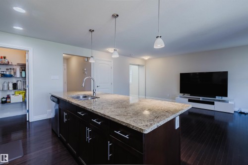 Spacious kitchen island featuring a granite countertop, stainless steel sink, and dark wood cabinetry with brushed nickel hardware - 17348 6 Avenue Nw, Edmonton, AB - Indoor Photo Showing Kitchen With Double Sink