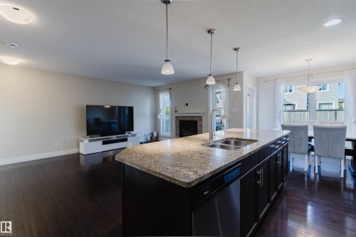 Open-concept living space featuring a kitchen island with stone countertop, dark wood-finish flooring, a stainless steel double sink, and pendant lighting - 17348 6 Avenue Nw, Edmonton, AB - Indoor Photo Showing Kitchen With Double Sink