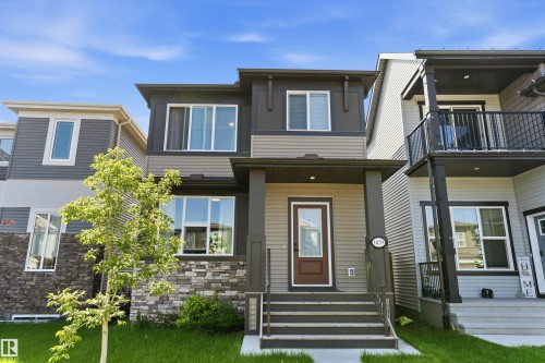 Modern multi-level exterior featuring light and dark gray siding, stone veneer accents, a covered front entry, and a prominent front door with a glass insert - 1439 Goodspeed Lane Nw, Edmonton, AB - Outdoor With Facade