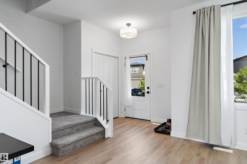 Foyer featuring light wood-finish flooring, a contemporary staircase with black wrought iron spindles, a white paneled front door with sidelight, a flush-mount ceiling light fixture, and a white bi-fold closet door - 1439 Goodspeed Lane Nw, Edmonton, AB - Indoor Photo Showing Other Room
