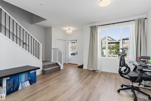 Open-concept entry foyer featuring wood-finish flooring, a contemporary staircase with black metal balusters, and a large window with ample natural light - 1439 Goodspeed Lane Nw, Edmonton, AB - Indoor Photo Showing Office