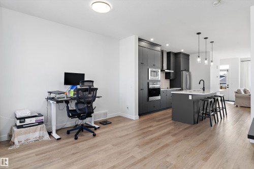 Open-concept living space featuring wood-finish flooring, a contemporary kitchen with dark cabinetry, stainless steel appliances, a center island with seating, and pendant lighting - 1439 Goodspeed Lane Nw, Edmonton, AB - Indoor Photo Showing Other Room