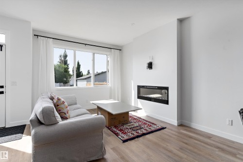 Bright living space featuring a built-in electric fireplace, large window with white curtain panels, wood-finish flooring, and white baseboards - 1439 Goodspeed Lane Nw, Edmonton, AB - Indoor Photo Showing Living Room With Fireplace