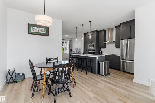 Open-concept kitchen and dining area featuring dark cabinetry, stainless steel appliances, a center island with seating, pendant lighting, and wood-finish flooring - 1439 Goodspeed Lane Nw, Edmonton, AB - Indoor