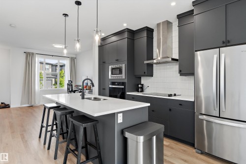 Modern kitchen featuring dark cabinetry, stainless steel appliances, a white quartz island with an undermount sink, and light wood-finish flooring - 1439 Goodspeed Lane Nw, Edmonton, AB - Indoor Photo Showing Kitchen With Double Sink With Upgraded Kitchen