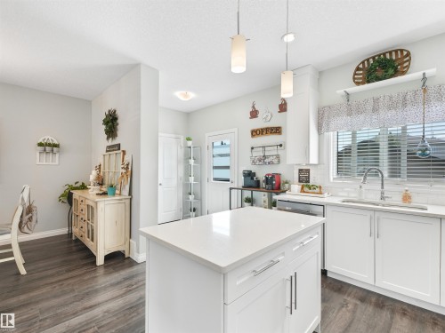 Kitchen featuring a central island with a solid surface countertop, white cabinetry with silver-tone hardware, wood-finish flooring, a white subway tile backsplash, and recessed and pendant lighting - 283 Ameena Drive, Leduc, AB - Indoor Photo Showing Kitchen