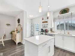 Kitchen featuring a central island with a solid surface countertop, white cabinetry with silver-tone hardware, wood-finish flooring, a white subway tile backsplash, and recessed and pendant lighting - 