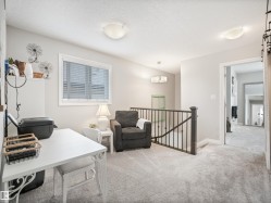 Carpeted upper-level landing featuring a large window with blinds, a dark wood newel post and balusters, and recessed lighting - 