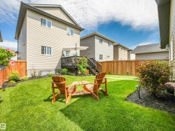 Expansive backyard featuring a manicured lawn, a wooden deck with stairs, mature privacy fencing, and landscaped garden beds - 