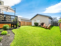 Spacious backyard featuring a large elevated deck, a detached garage, a storage shed, a manicured lawn, and perimeter wood fencing - 