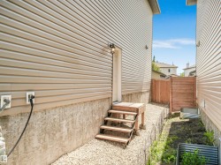 Exterior side access with steps and a wooden privacy fence, featuring beige horizontal siding and a gravel pathway - 