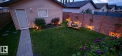 Private backyard featuring a manicured lawn, established shrubs, and a paved walkway leading to a rear outbuilding - 